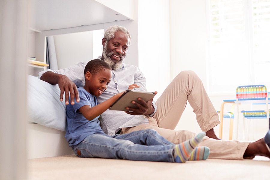 Client Center - Grandfather with Grandson Looking at a Tablet on Grandson’s Bedroom Floor