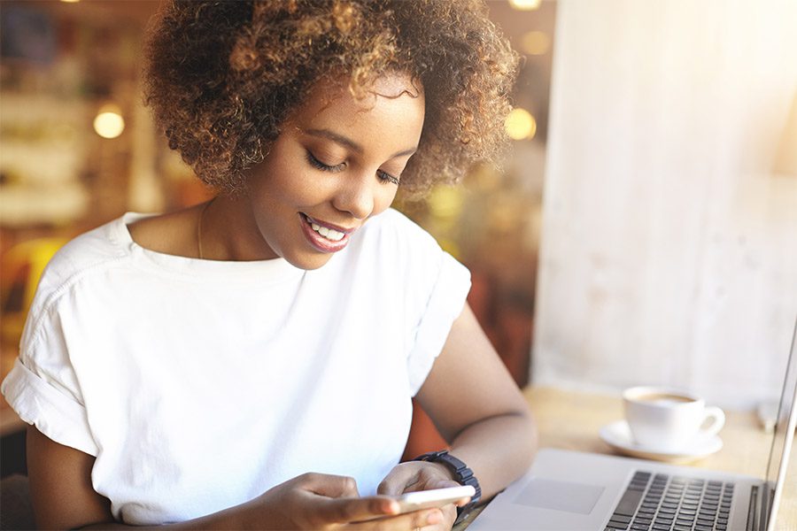 Video Library - Woman Holding Smart Phone Sitting in Front of Laptop at a Cafe